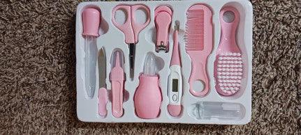 A pink baby care kit featuring thermometer, nasal inhaler, safety nail clippers, comb, and brush designed for grooming and caring for infant.