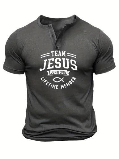 The image shows a dark gray men's short-sleeve T-shirt with a buttoned Henley-style collar. The shirt features a bold white graphic design on the front that reads "TEAM JESUS" with "JOHN 3:16" positioned underneath, referring to the Bible verse. Below this, the phrase "LIFETIME MEMBER" is curved around a Christian ichthys symbol, commonly known as the "Jesus fish." The shirt has a fitted style, emphasizing a casual yet faith-based statement through its design.