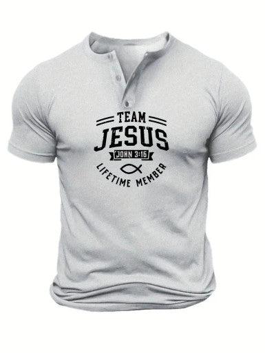 The image features a white, short-sleeve Henley-style shirt with a three-button placket. The shirt has a bold, black design in the center that reads "TEAM JESUS" with "John 3:16" written below it. Underneath, there is a Christian fish symbol followed by the words "LIFETIME MEMBER." The shirt is fitted, emphasizing the muscular build of the person wearing it.