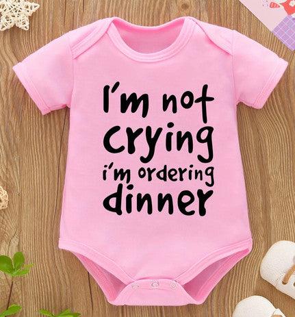 A pink baby girl snap-bottom onesie with the playful message 'I'm Not Crying, I'm Ordering Dinner,' perfect for adding a touch of humor and style to your little one's wardrobe.