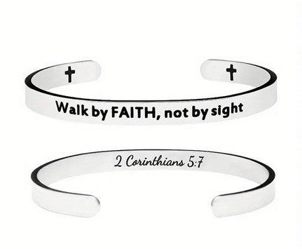 Silver cuff bracelet engraved with the phrases "Walk by FAITH, not by sight" on the outside and "2 Corinthians 5:7" on the inside. The bracelet also features small cross symbols near the open ends.