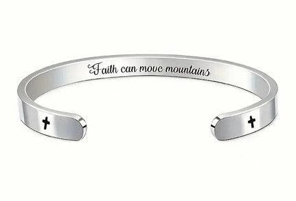 Silver cuff bracelet engraved with the phrase "Faith can move mountains" on the outside. The bracelet also features small black cross symbols near the open ends.