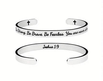 Silver cuff bracelet engraved with the phrase "Be Strong, Be Brave, Be Fearless. You are never alone" on the outside and "Joshua 1:9" on the inside. The bracelet also features small cross symbols near the open ends.