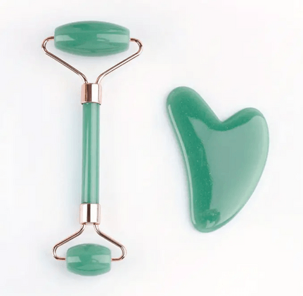 A jade roller and gua sha set, both made from smooth green jade stone. The jade roller features two rolling ends of different sizes, attached to a metal frame with a matching green handle, designed for facial massage to promote circulation and reduce puffiness. The gua sha tool has a heart-shaped design, ideal for contouring and massaging the face. The set combines beauty and wellness, offering a natural method for skin care and relaxation.