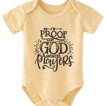 Yellow baby onesie with the phrase "I'm proof that God answers prayers" printed in bold black lettering. The design includes decorative accents like arrows and rays surrounding the text. The onesie has short sleeves and a snap closure at the bottom for easy dressing.