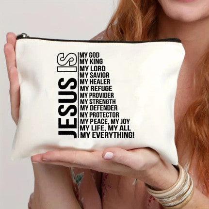 A white canvas pouch with bold black text that reads: "JESUS IS" vertically on the left, followed by a list of attributes in a smaller font: "My God, My King, My Lord, My Savior, My Healer, My Refuge, My Provider, My Strength, My Defender, My Protector, My Peace, My Joy, My Life, My All, My Everything!" The pouch features a black zipper and is held by a person, highlighting its size and design. This faith-themed accessory is ideal for storing personal items or as a meaningful gift.