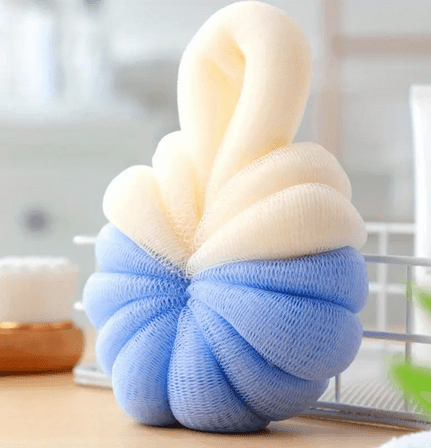 A dual-colored bath sponge with a soft, textured mesh design. The sponge features a top half in cream and a bottom half in light blue, twisted together to form a plump, round shape. The sponge has a loop at the top, allowing it to be easily hung for drying. This bath accessory is designed for gentle exfoliation and cleansing during showers or baths, adding a touch of color and comfort to the bathing experience.