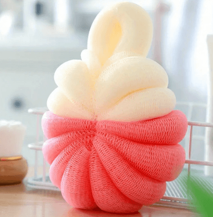 A two-tone bath sponge with a soft, textured mesh design. The sponge features a top half in cream and a bottom half in pink, twisted together into a rounded, plump shape. It includes a loop at the top for easy hanging and drying. This bath accessory is ideal for gentle exfoliation and cleansing during showers or baths, providing a pop of color and comfort to your bathing routine.